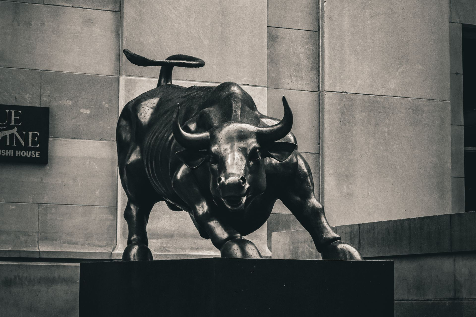 Black-and-white photograph of a charging bull statue on a stone pedestal